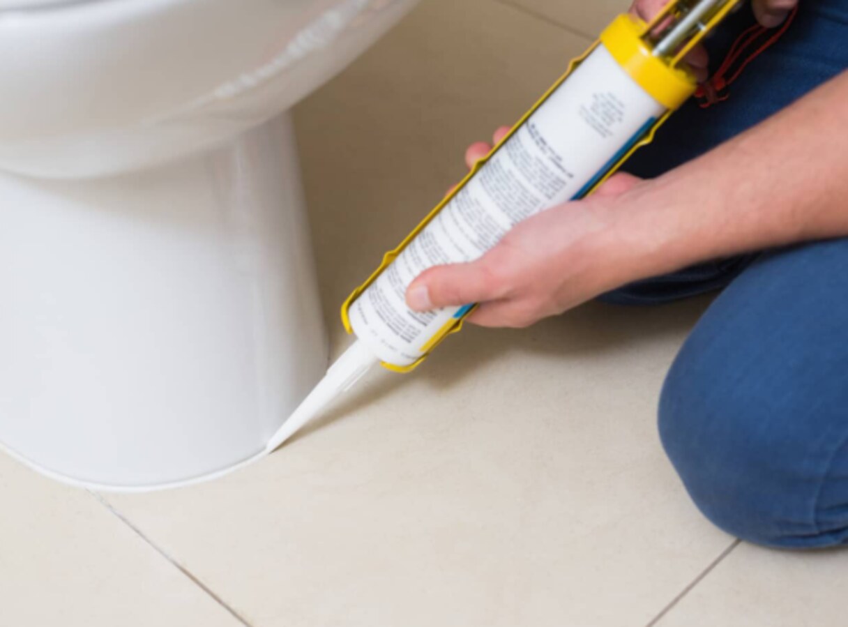 Plumber applying silicone sealant around the base of a toilet